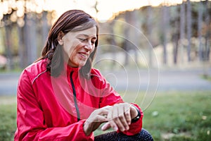 A female runner outdoors in autumn nature, checking the time.