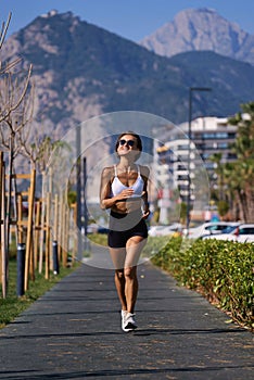 Female runner running at morning in city park. Healthy fitness woman jogging outdoors. Mountains in background.