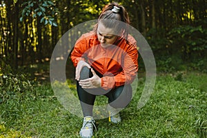 Female runner suffering with pain on sports running knee injury in nature. Person with backpack walking in the forest