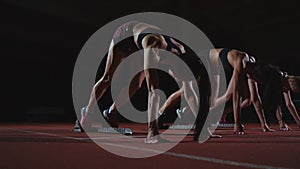 Female runners at athletics track crouching at the starting blocks before a race. In slow motion.