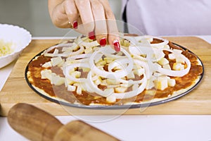 Female`s hand adds slices of onion for pizza photo