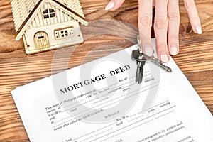 Female`s hand giving mortgage deed and keys from house over table. Real estate concept