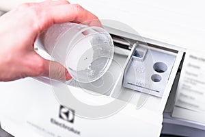 Female's hand pouring washing powder detergent into washing machine.