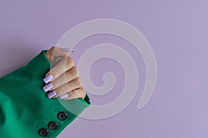 Female\'s hand with purple nails wearing green jacket on purple background photo