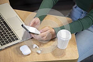 Female`s hands with cell phone in front of laptop computer, sits at cafeteria, surrounded with mug of coffee and modern laptop photo