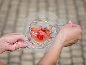 A female`s hands with a cup of berries liquid on a stone blurred background. Delicious and natural strawberry tea.