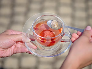 A female`s hands with a cup of berries liquid on a stone blurred background. Delicious and natural strawberry tea.