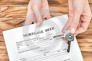 Female's hands giving mortgage deed and keys from house over table. Real estate concept