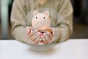 A female`s hands holding a piggy bank and coins over the table. Saving money, financial