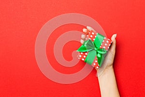 Female`s hands holding striped gift box with colored ribbon on red background. Christmas concept or other holiday handmade presen