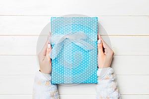 Female`s hands holding striped gift box with colored ribbon on white rustic wooden background. Christmas concept or other holiday