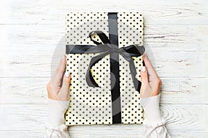 Female`s hands holding striped gift box with colored ribbon on white rustic wooden background. Christmas concept or other holiday