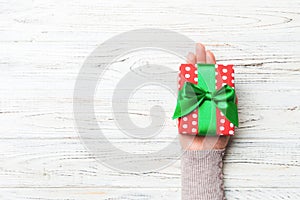 Female`s hands holding striped gift box with colored ribbon on white rustic wooden background. Christmas concept or other holiday