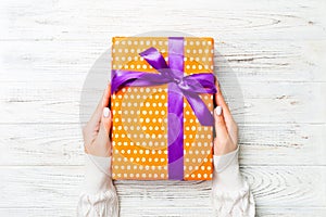 Female`s hands holding striped gift box with colored ribbon on white rustic wooden background. Christmas concept or other holiday