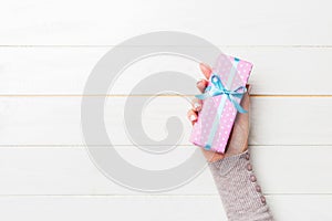 Female`s hands holding striped gift box with colored ribbon on white rustic wooden background. Christmas concept or other holiday