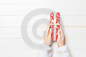 Female`s hands holding striped gift box with colored ribbon on white rustic wooden background. Christmas concept or other holiday