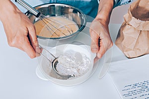 Female`s hands scoop flour in sieve to sift it into the dough photo