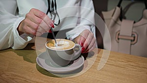 Female`s hands with spoon cappuccino, close-up. Young woman drinking coffee