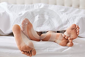 Female`s and male`s bare feet have rest under white blanket, rec