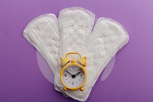 Female`s menstrual cycle concept. Sanitary pads with yellow alarm clock