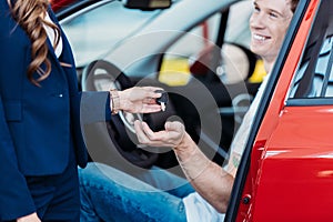 Female sales manager giving a car key to smiling male customer in a