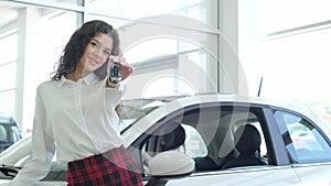 A female saleswoman shows the keys to a new car at a car dealership.