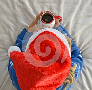 Female in a Santa Claus hat relaxing and drinking morning coffee in bed at home