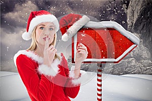 Female santa with finger on lips standing in snowfall