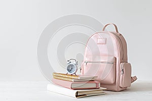 Female school backpack with stationery supplies on desk at white loft brick. Back to school concept