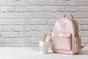 Female school backpack with stationery supplies on desk at white loft brick. Back to school concept