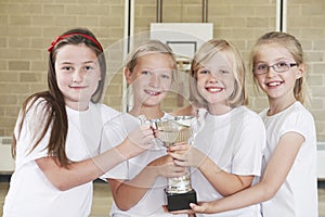 Female School Sports Team In Gym With Trophy