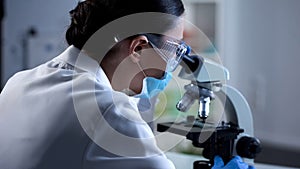 Female scientist analyzing sample under microscope, microbiology research