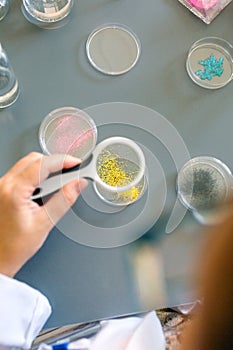 Female scientist examining golden glitter sample through a magnifying glass on pharmaceutical lab