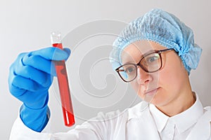 A female scientist with glasses is conducting an experiment in a laboratory, holding a test tube with red liquid in her hands