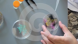 Female scientist hands shaking petri dish with glitters mix sample and analysis liquid in lab