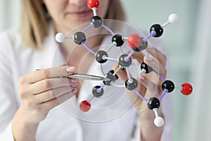 Female scientist holds model of molecular structure and points to one molecule close-up.
