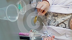 Female scientist pouring liquid from from pipette over petri dish with golden glitter sample in lab