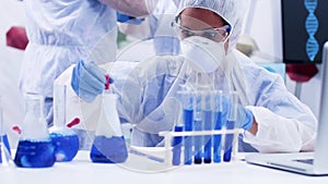 Female scientist in protection gear using a pipette to take a sample of smoking blue fluid