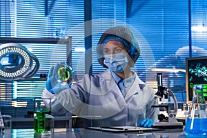 Female scientist sitting in a research lab. A female doctor in a white coat examining a sample of green biomaterial in a