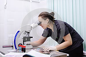 Female scientist studying new substance or virus in microscope