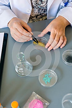 Female scientist with tweezers analyzing golden glitter sample over petri dish on research lab