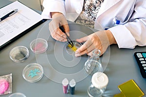 Female scientist with tweezers examining golden glitter sample over petri dish on research lab