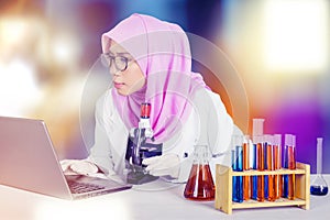 Female scientist using laptop and microscope