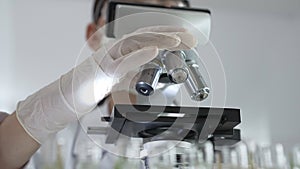Female scientist wearing white protective gear analyzing test samples under microscope in contemporary research