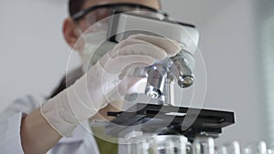 Female scientist wearing white protective gear analyzing test samples under microscope in contemporary research