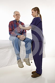 Female in scrubs listening to elderly man's heart.