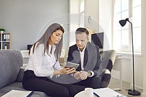 Female secretary with digital tablet in hands shows electronic documents to her boss.