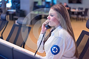 Female security guard operator talking on the phone, calling in the alarming event to the external team of field force agents