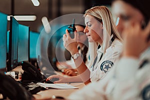 Female security operator holding portable radio in hand while working in a data system control room offices Technical