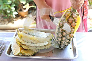 Female seller's hands using a knife to pare pineapple photo